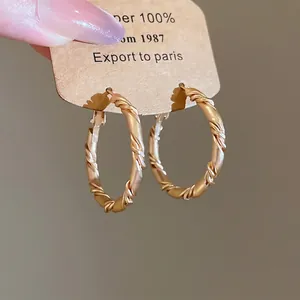 Elegant gold twisted hoop earrings with woven texture on a minimalist display card