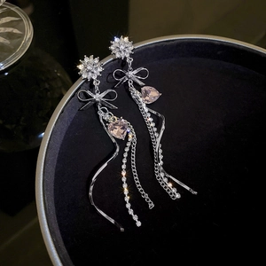 Close-up of silver long tassel earrings with a bow, sparkling crystals and heart pendant