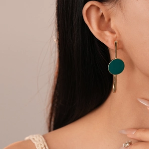 Détail d'une boucle d'oreille pendante dorée avec cercle en émail vert sur un modèle