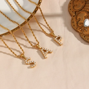 Detailed macro of gold twist chain with pearl-inlaid S, A, and P letter pendants