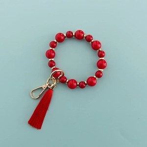 Détail d'un porte-clés bracelet en perles rouges avec accents dorés et pompon rouge