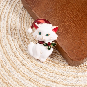 Macro detail of Christmas white cat enamel brooch with red Santa hat and green rhinestones