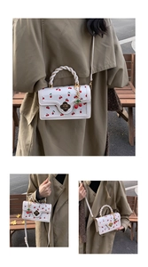 Detail of white cherry print handbag with braided handle and floral metal clasp