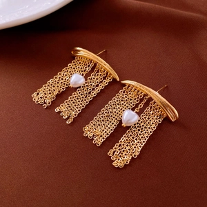 Detail view of gold tassel earrings with heart-shaped pearl on dark velvet background