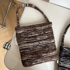 Detail of a brown and navy woven tote bag featuring a white Simple Wish brand label
