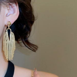 Detail of gold tassel earrings with spherical studs and multi-layer chain fringe