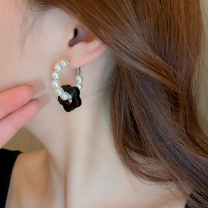 Close-up of pearl hoop earrings featuring a black flower pendant on a model