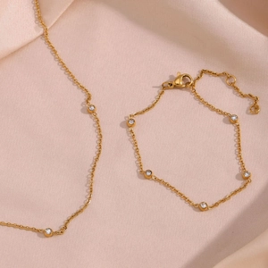Detail of gold chain necklace and bracelet set with cubic zirconia on pink silk fabric