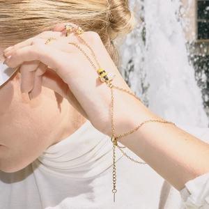 Detail eines goldenen Bienen-Handschmucks mit Blumenring und Emaille-Biene am Modell