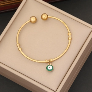 Gold stainless steel evil eye cuff bracelet with green enamel charm on jewelry box