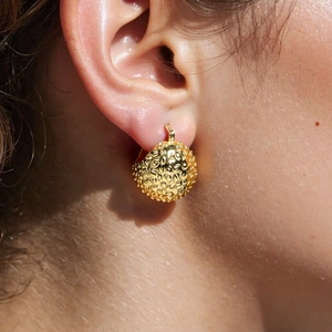 Close-up of golden spherical earrings with relief texture worn on earlobe