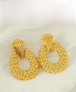 Détail des boucles d'oreilles ananas en or mat sur un tissu élégant en soie blanche