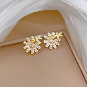 Macro detail of gold flower and butterfly stud earrings with clear crystals on a jewelry box
