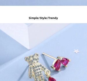 Detail of asymmetric bear stud earrings with red heart stones on blue texture