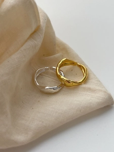 Close-up of gold and silver wavy irregular rings on a natural beige linen fabric background