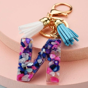 Detailed view of resin letter N keychain with colorful stones and soft fabric tassels