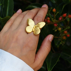 Exaggerated 3D butterfly open ring in gold plated copper on finger with nature background