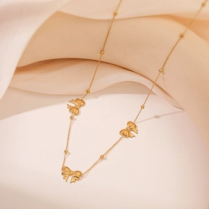 Elegant gold bow pendant necklace with small beads on soft beige silk fabric