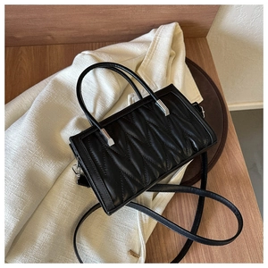 Close-up of black quilted handbag with M-pattern texture on a white coat and wooden surface