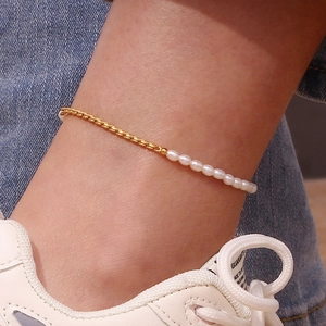 Detail einer minimalistischen Goldkette und Süßwasserperlen-Fußkette am Knöchel