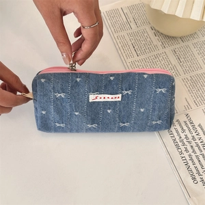 Detail of hand pulling a pink zipper on a blue denim stationery pouch with bow patterns