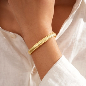 Close-up of 18k gold plated bracelet with geometric woven texture on female wrist