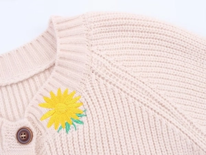 Detail of cream knit cardigan with yellow sunflower embroidery and brown button