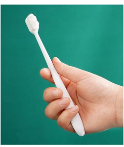 Close-up of white nano soft bristle toothbrush held by hand on green background
