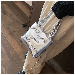 Detail of silver metallic square bag with decorative 3D bows and chain strap