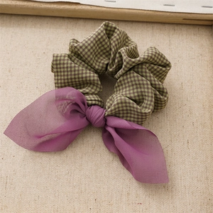 Detail view of a plaid fabric scrunchie with a purple chiffon bow on a beige surface