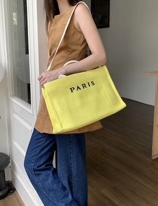 Close-up of bright yellow woven straw tote bag with black Paris print on shoulder