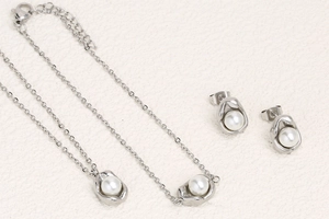 Detailed view of silver pea-shaped necklace and pearl earrings set on leather surface