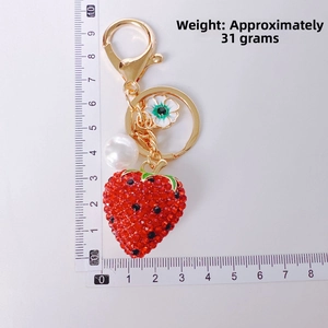 Detail view of strawberry keychain with red rhinestones, white pearl, and enamel flower