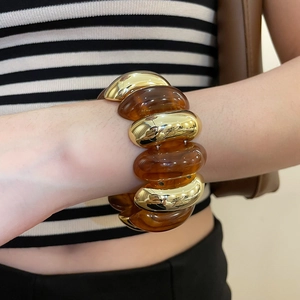 Detail of chunky gold chain bracelet with amber acrylic resin links worn by a model