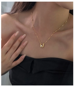Detailed view of horseshoe pendant with pearl on a gold chain worn by a model