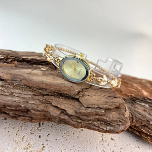 Detailed view of luxury gold oval quartz watch with stone-set leaf-style bracelet on wood