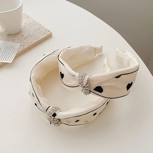 Detail of white fabric headbands featuring black heart patterns and rhinestone knots