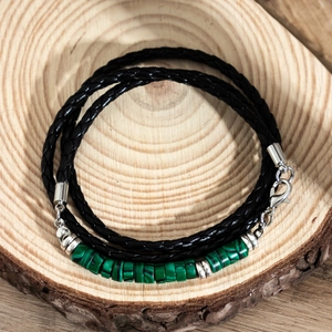 Men's braided black leather bracelet with green malachite beads on a wooden base