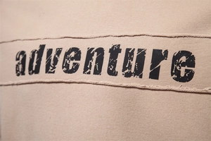 Detail of adventure print and raw edge patchwork on khaki long sleeve sweatshirt