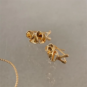 Close-up of golden wavy heart stud earrings with abstract pleated texture on a grey surface