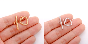 Macro view of gold and silver heart-shaped OT toggle clasps held in hand for jewelry DIY