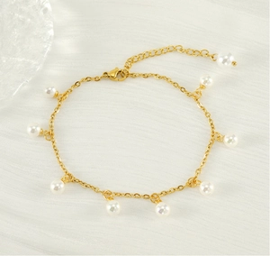 Detailed macro view of 18K gold tassels and white pearls on the anklet over textured fabric
