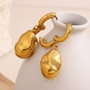 Detailed view of polished gold peanut pendant earrings on a minimalist white ceramic vase