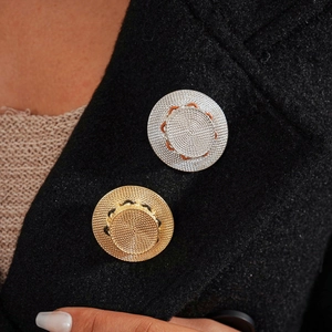 Close-up of metallic hat brooch with woven texture pinned on a black wool coat