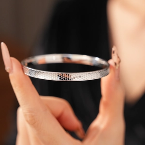 Detailed close-up of a silver metal bangle featuring a honeycomb texture and beaded edges
