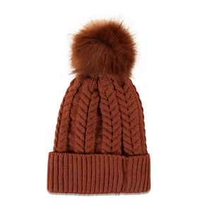 Close-up of caramel cable knit beanie featuring a fluffy faux fur pompom and ribbed cuff