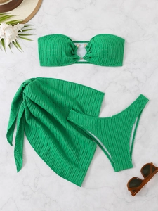 Flat lay of emerald green three-piece bikini set with gold ring detail and sarong wrap