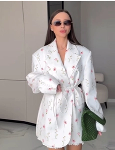 Dettaglio di blazer bianco con stampa floreale rosa e cintura sottile sul modello
