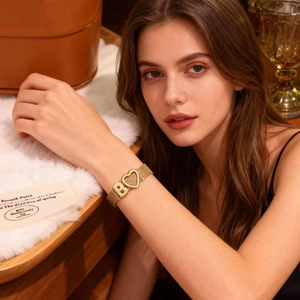 Détail d'un bracelet en maille dorée avec charms cœur et lettre B porté au poignet