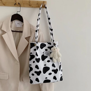 Cow print canvas tote bag with bear plush charm hanging on a wooden hook scene